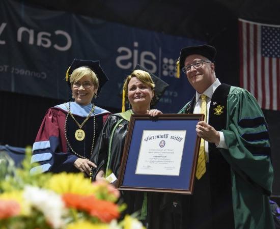 职业治疗学教授 Mary Siniscaro stands between Provost Todd Pfannestiel and President Laura Casamento, 在2023年本科毕业典礼上颁奖.